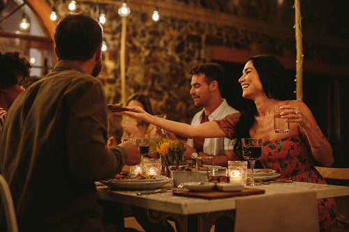 Woman passing food to friends at dinner party