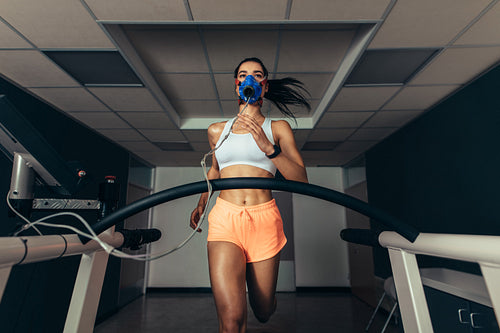 Fit woman running on treadmill with a mask