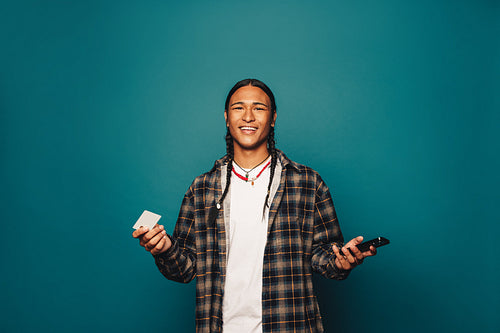 Cheerful man smiling and paying with premium credit card via online banking on a blue studio background