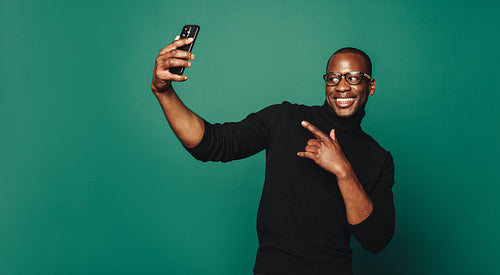 Stylish casual man posing with smartphone for selfie on green background