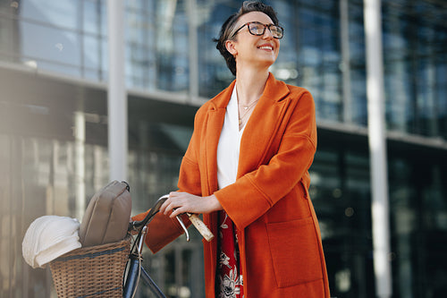 Happy businesswoman looking away while pushing her bike in the city