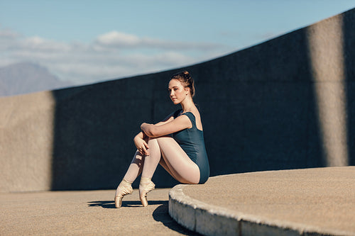 Female ballet dancer sitting gracefully while resting her toes on the ground