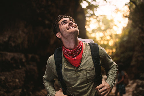Smiling young guy hiking in mountain and looking up