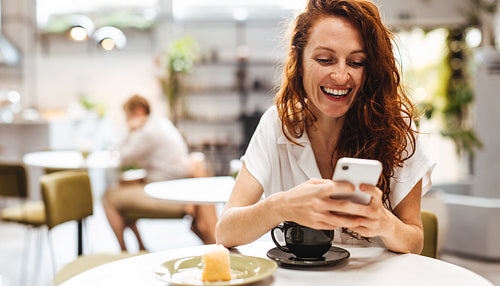 Woman sitting in a cafe and texting her friends with her phone