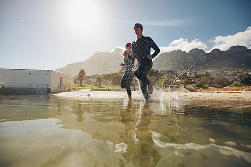 Two competitors in wet suits running into the water