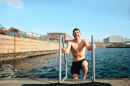 A ladder helps the man continue swimming as he climbs from the cold water by the dock.