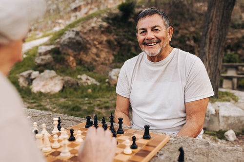 Happy senior man playing chess with his wife outdoors