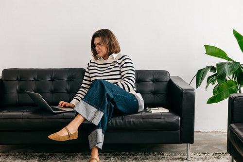 Laptop work keeps the woman focused at home on a sofa