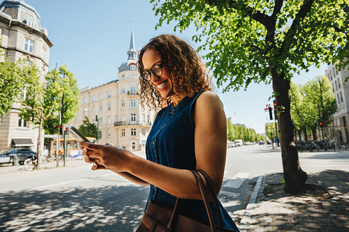 Cheerful woman using a smartphone app on a tree-lined city boulevard in summer