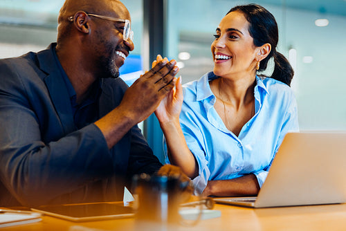 Two colleagues exchanging a high five during a conversation in an office setting