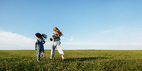 Children running across open field under clear blue sky