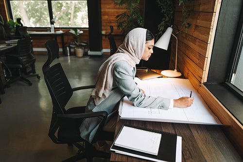 Creative Muslim designer working with blueprints in an office