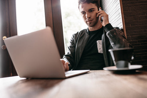 Man at cafe working on laptop and mobile phone