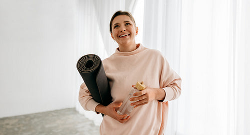 Woman with a yoga mat and water bottle, she begins her fitness routine at home