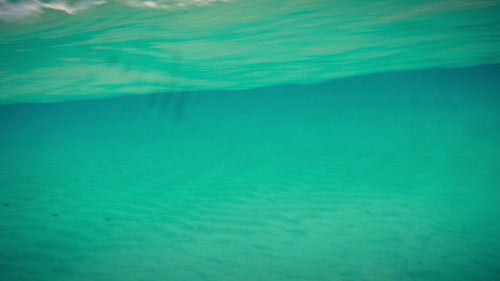 Clear turquoise ocean water view from underwater showing waves and sandy seabed