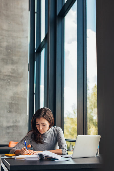 Student taking notes from books at library