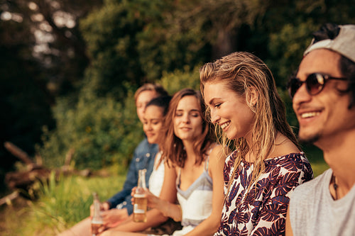 Happy young woman sitting with her friends by a lake