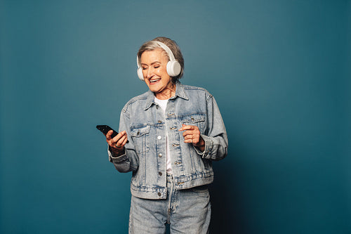 Happy mature woman listening to music with headphones and a smartphone