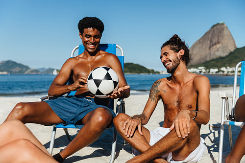 Friends enjoying a sunny day at the beach with laughter and a soccer ball