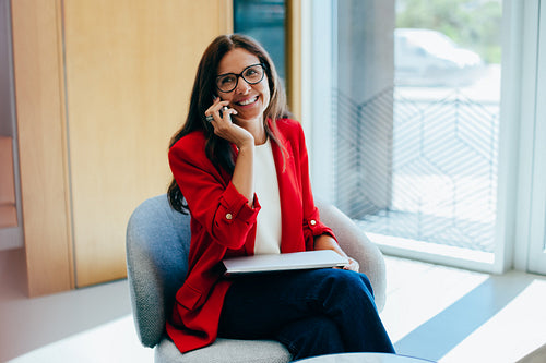 Businesswoman in red blazer engaging in a phone call while seated indoors