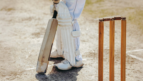 Cricketer preparing to bat near stumps on a sunny day