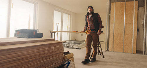 Male construction worker in a home kitchen, looking at camera with tool belt
