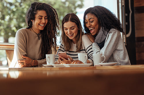 Friends sitting in a cafe looking at mobile phone