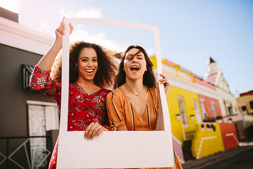 Excited women outdoors with a photo frame