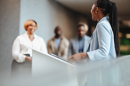 Young businesswoman and speaker delivering presentation from a podium at corporate meeting