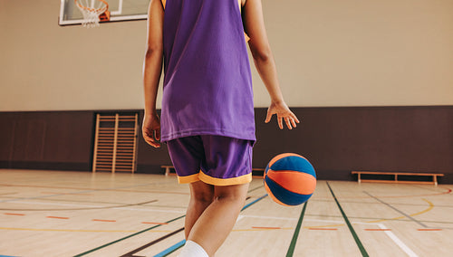 Young athlete dribbling basketball on indoor court in sports attire