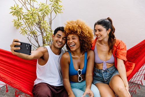 Three friends taking a selfie while relaxing together outdoors on a sunny day