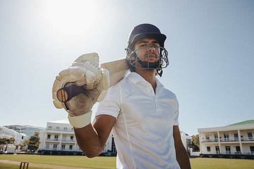 Portrait of a male cricket player carrying a bat on his shoulder under bright sunlight