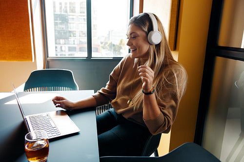 Young woman listening to music while working on laptop in modern office