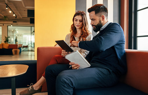Two focused businesspeople using a digital tablet in a lobby