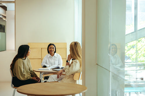Urban students engage in teamwork during a group discussion at a modern indoor cafe setting, fostering collaboration and connection.