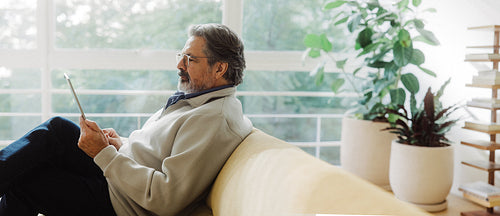Senior man uses a tablet while sitting at home