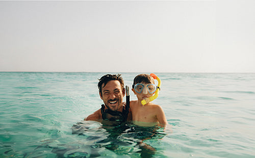 Father and son snorkeling with goggles and smiling in the clear sea