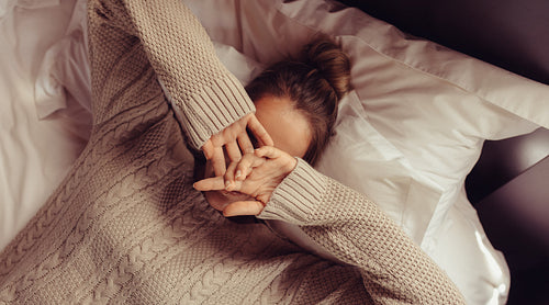 Woman lying on bed with hands covering face
