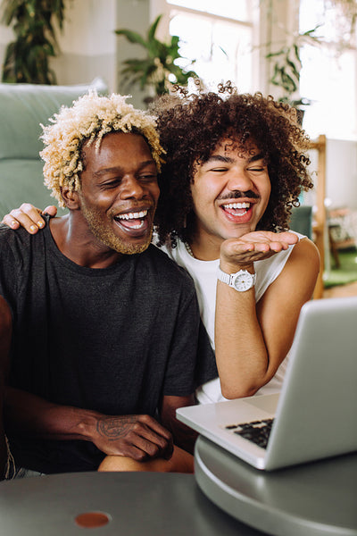 Happy gay couple video calling their friends on a laptop