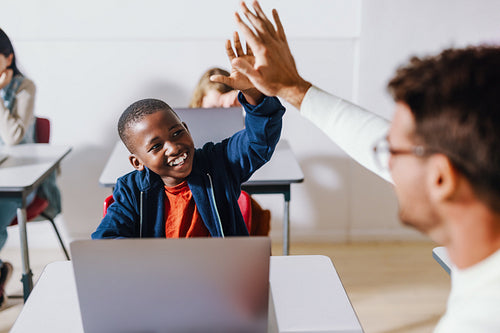 Teacher and student doing a high five in a computer science classroom, celebrating a successful lesson