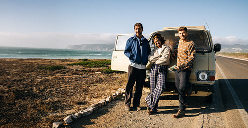 Friends on a coastal road trip pose by a vintage van along the seaside highway