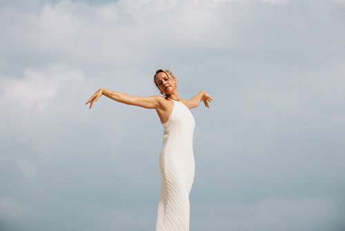 Elegant woman in white dress posing outdoors under a cloudy sky