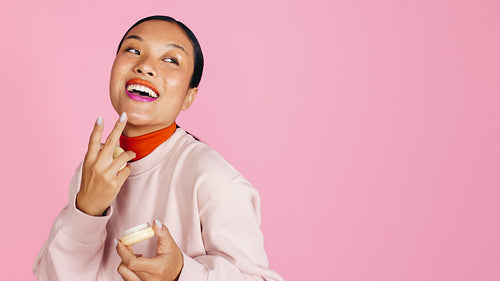 Happy woman applying cream foundation to her face in a studio