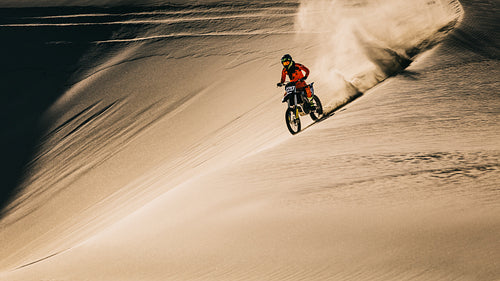 Dirt biker driving fast over dunes