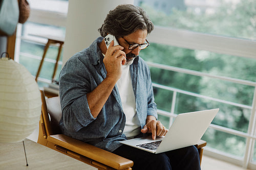 Senior man makes a phone call beside a laptop