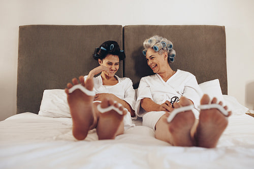 Mother and daughter sitting on bed wearing toe separator for pedicure