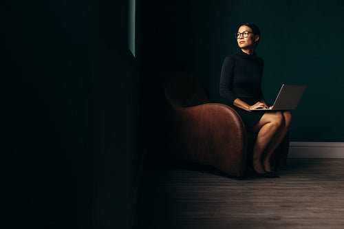 Thoughtful lady sitting on armchair with laptop