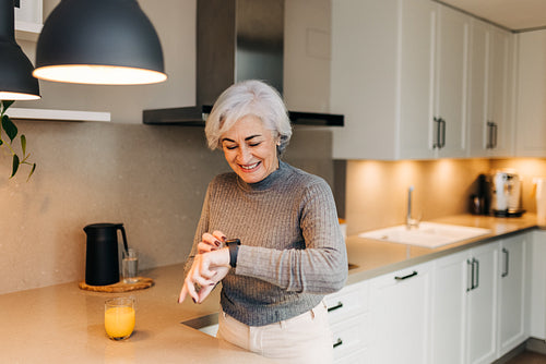 Healthy senior woman smiling at her smartwatch in her kitchen
