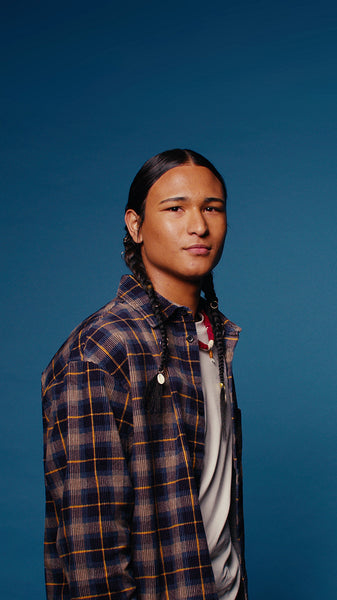 Young man with braided hair smiles for a studio portrait against a blue background