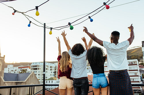 Young people partying on terrace with drinks at sunset